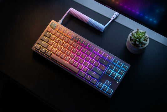 A vibrant mechanical keyboard with colorful RGB lighting sits at the center of a stylishly arranged gaming desk, surrounded by peripherals and glowing in a blend of warm and cool tones.